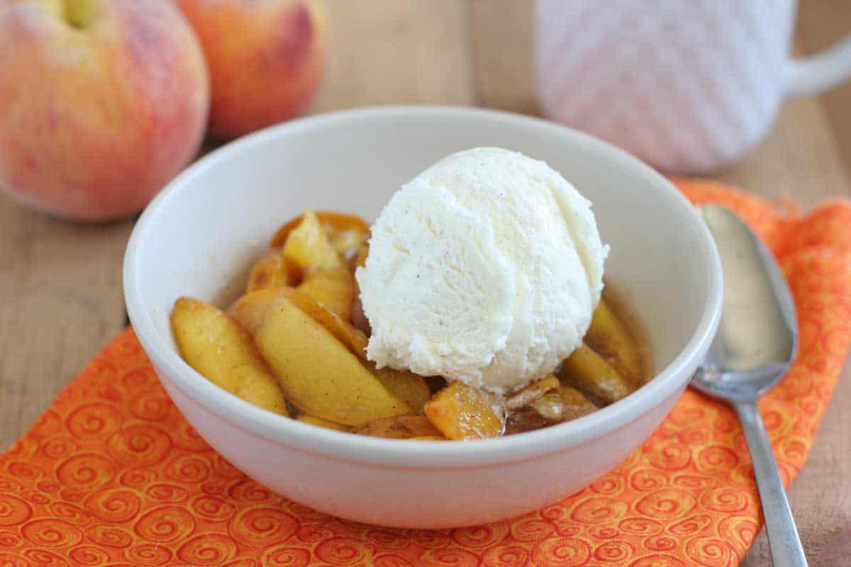A simple summer dessert, these Crock Pot Peaches are cooked slowly until warm, tender, and sweet. Top with ice cream for the ultimate taste of summer! bowl of Crock Pot Peaches topped with vanilla ice cream