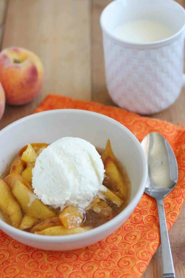 bowl of warm peaches cooked in the slow cooker topped with ice cream