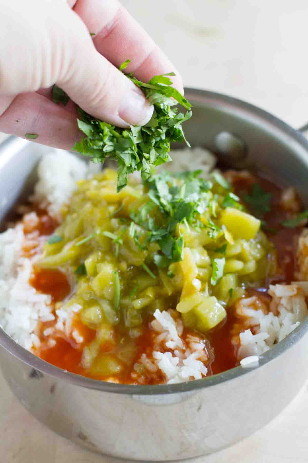Adding cilantro to a pot with rice, enchilada sauce, and green chiles.