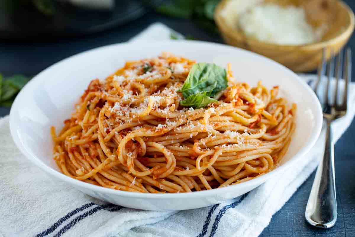 bowl filled with garlic spaghetti that is topped with parmesan and basil