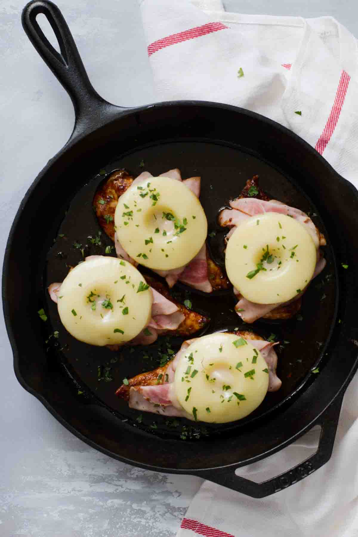 Hawaiian chicken topped with ham and pineapple in a cast iron pan.