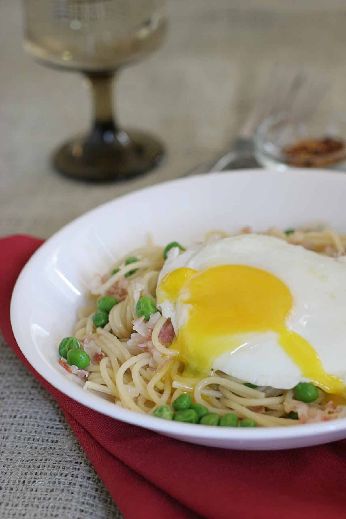 bowl of pancetta pasta with peas with an egg on top.
