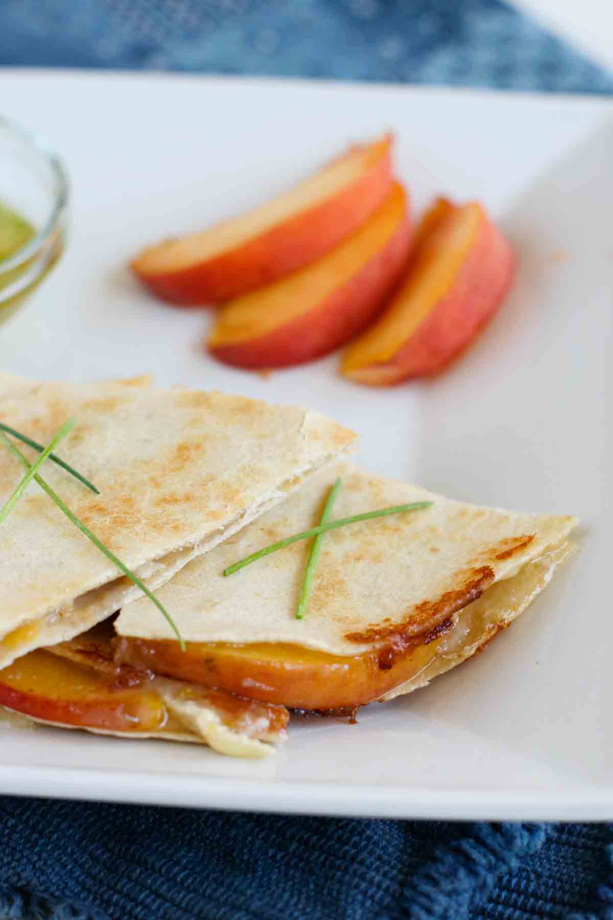 Peach and Brie Quesadillas on a plate with sliced peaches.