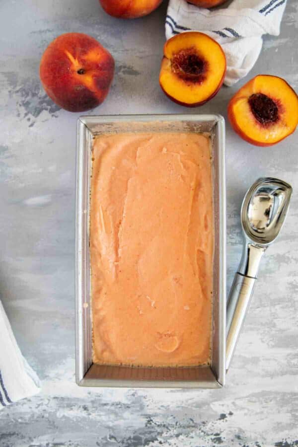 peach frozen yogurt in a stainless steel pan with fresh peaches