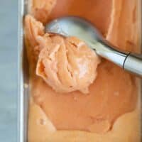 scooping peach frozen yogurt from a metal pan