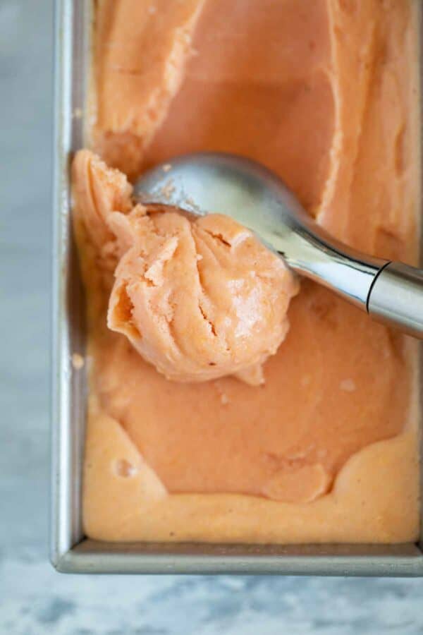 scooping peach frozen yogurt from a metal pan
