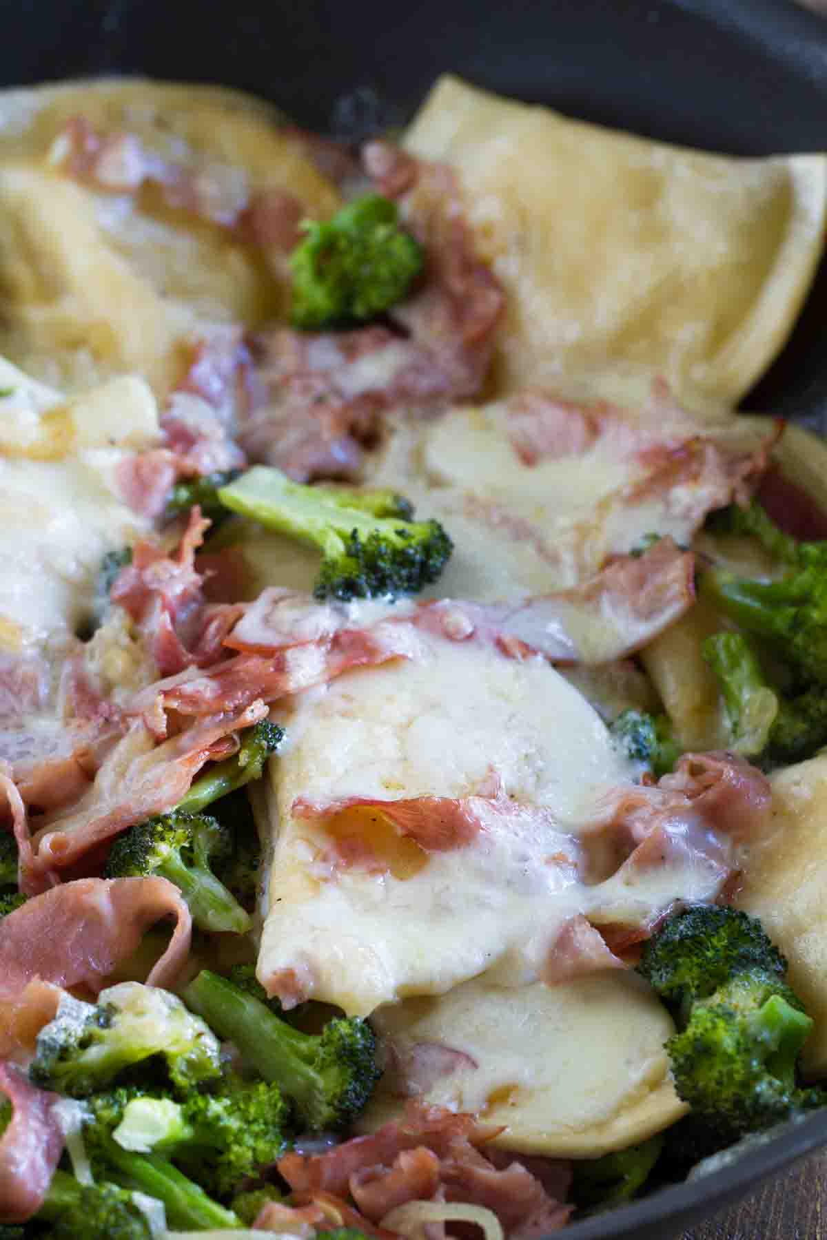 Pierogies with cheese, ham, and broccoli in a skillet.
