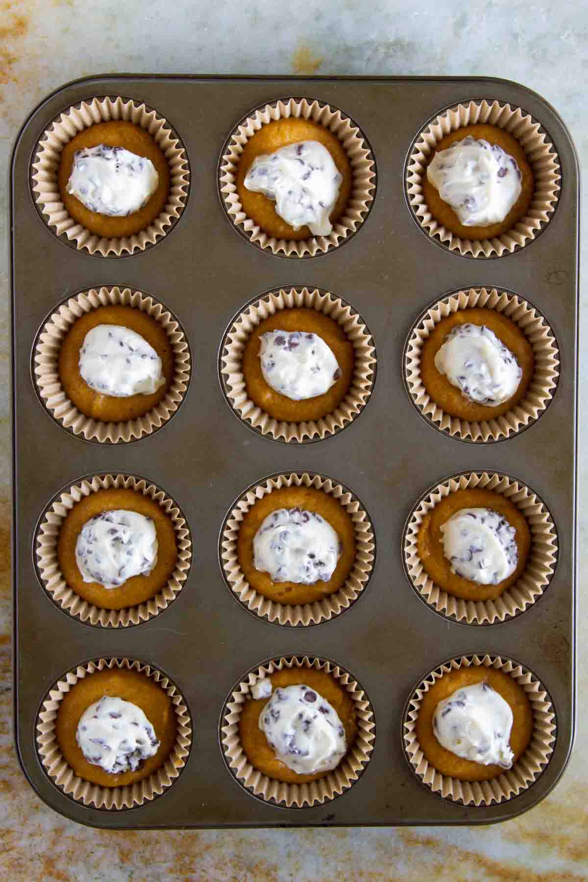 muffin tin filled with batter for pumpkin cheesecake spider cupcakes.