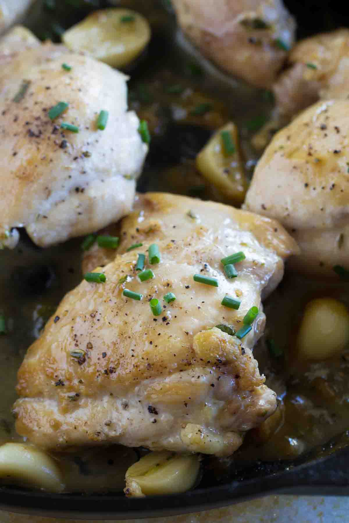 Chicken thigh cooked in a cast iron skillet topped with chives.
