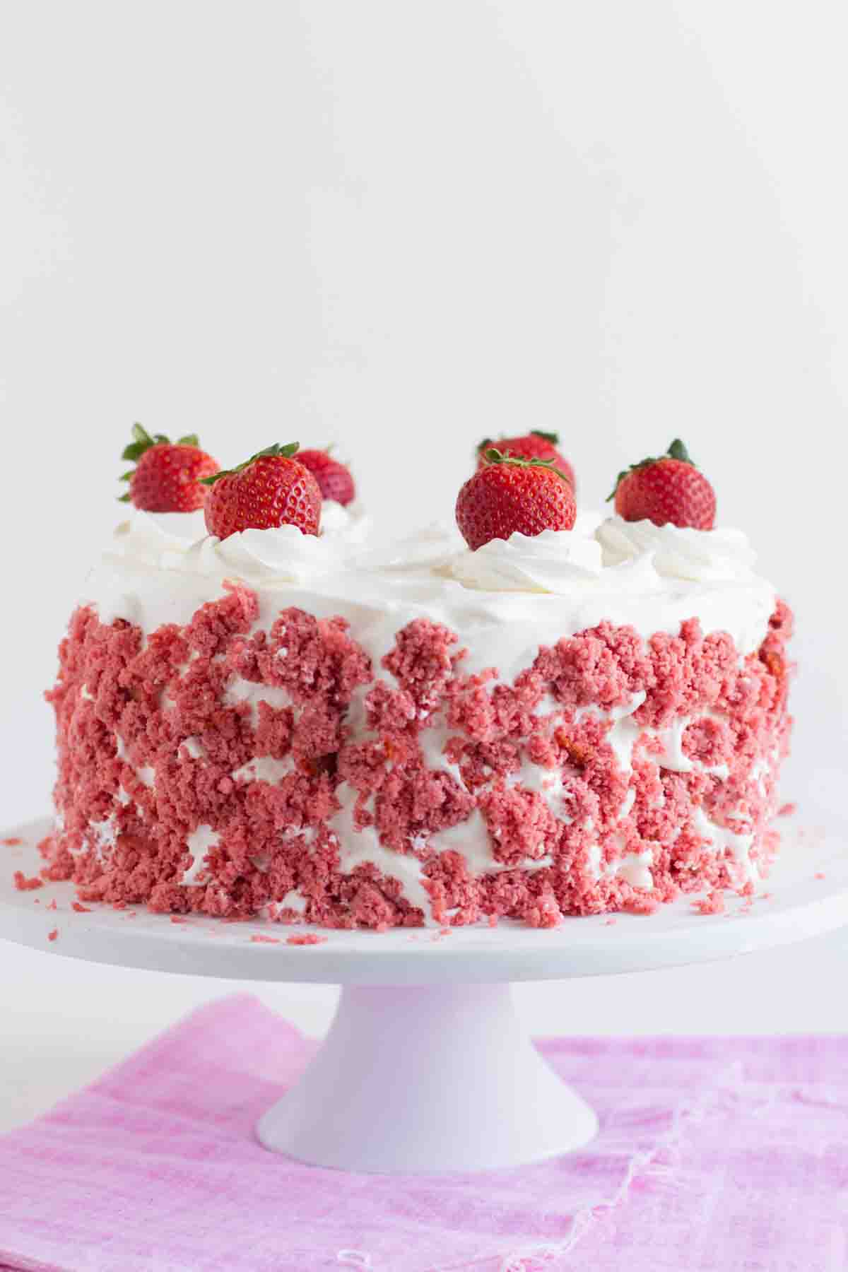 This Strawberry Milkshake Ice Cream Cake consists of layers of strawberry cake that are sandwiched with strawberry ice cream and frosted with sweetened whipped cream. It is such a delicious and fun ice cream cake! Full Strawberry Milkshake Ice Cream Cake on a cake stand topped with fresh strawberries.