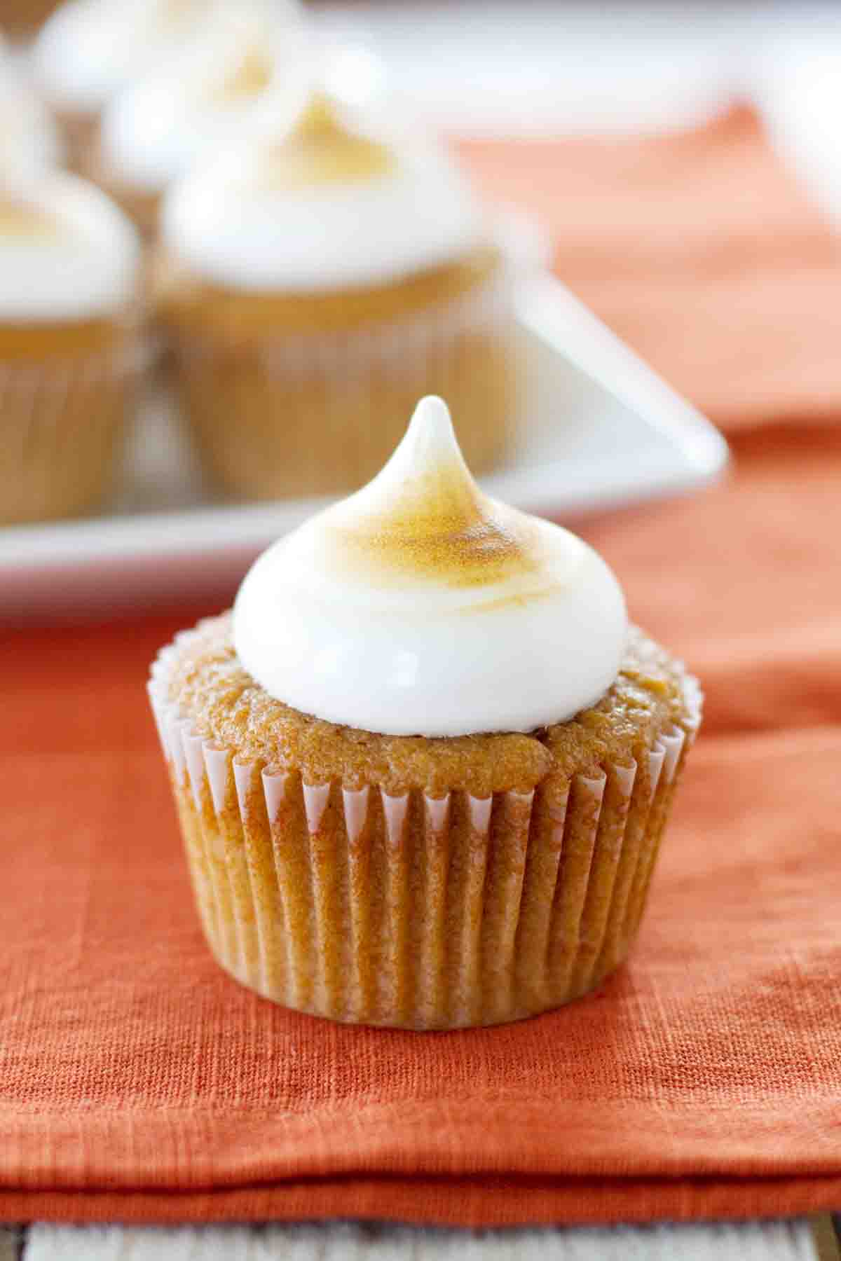 A single sweet potato cupcake on a linen with more cupcakes in the background.