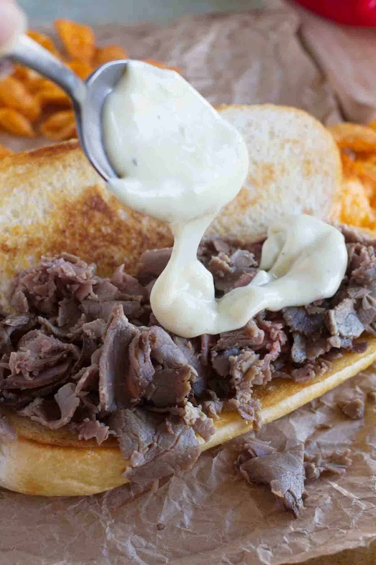 pouring cheese sauce over roast beef for a cheesesteak sandwich.