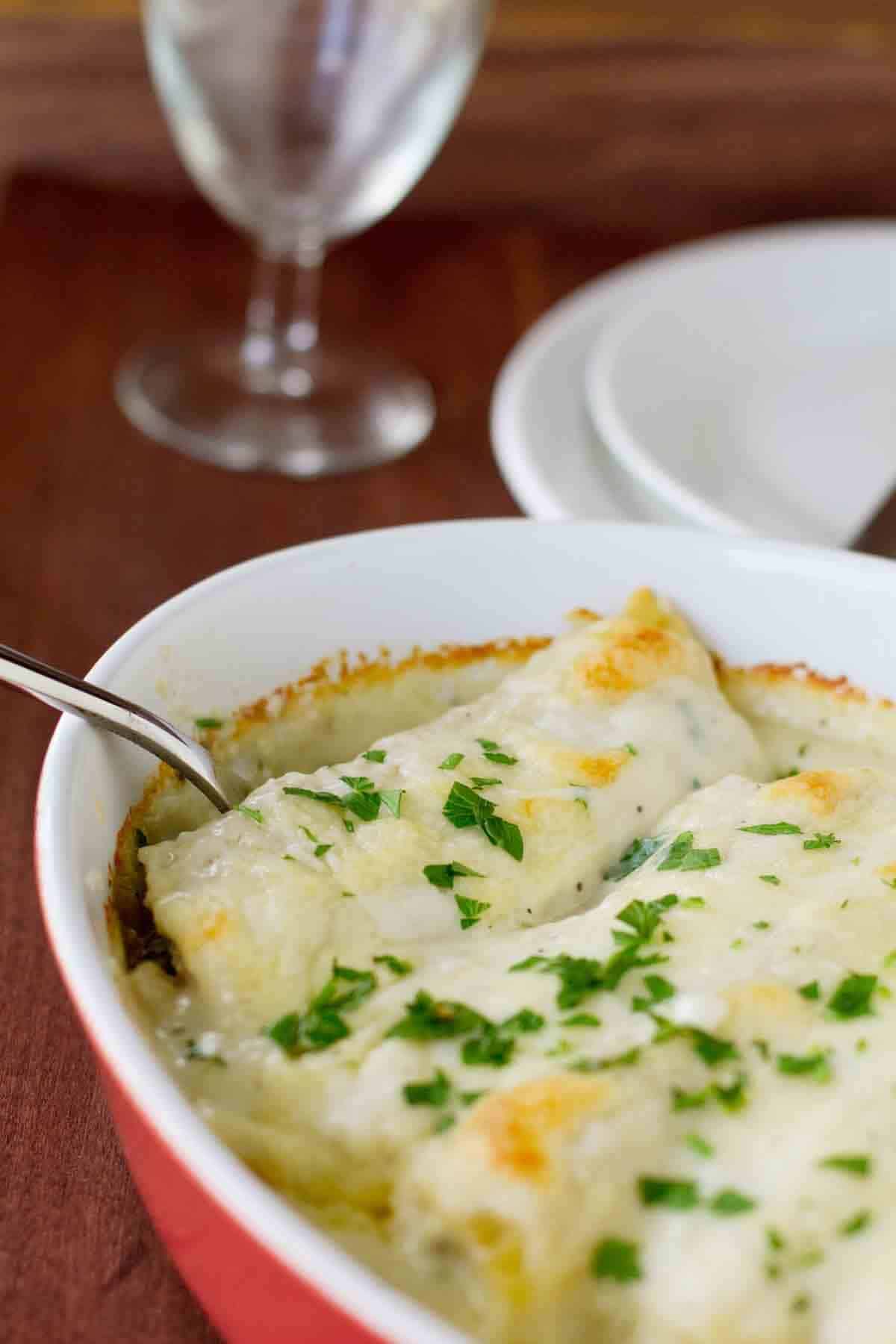 If you love manicotti, you’ll die over this Chicken Manicotti with Mushrooms. A delicious chicken and mushroom mixture is stuffed in manicotti shells and serve with a creamy white sauce that is irresistible. Baking dish with Chicken Manicotti with Mushrooms topped with parsley.