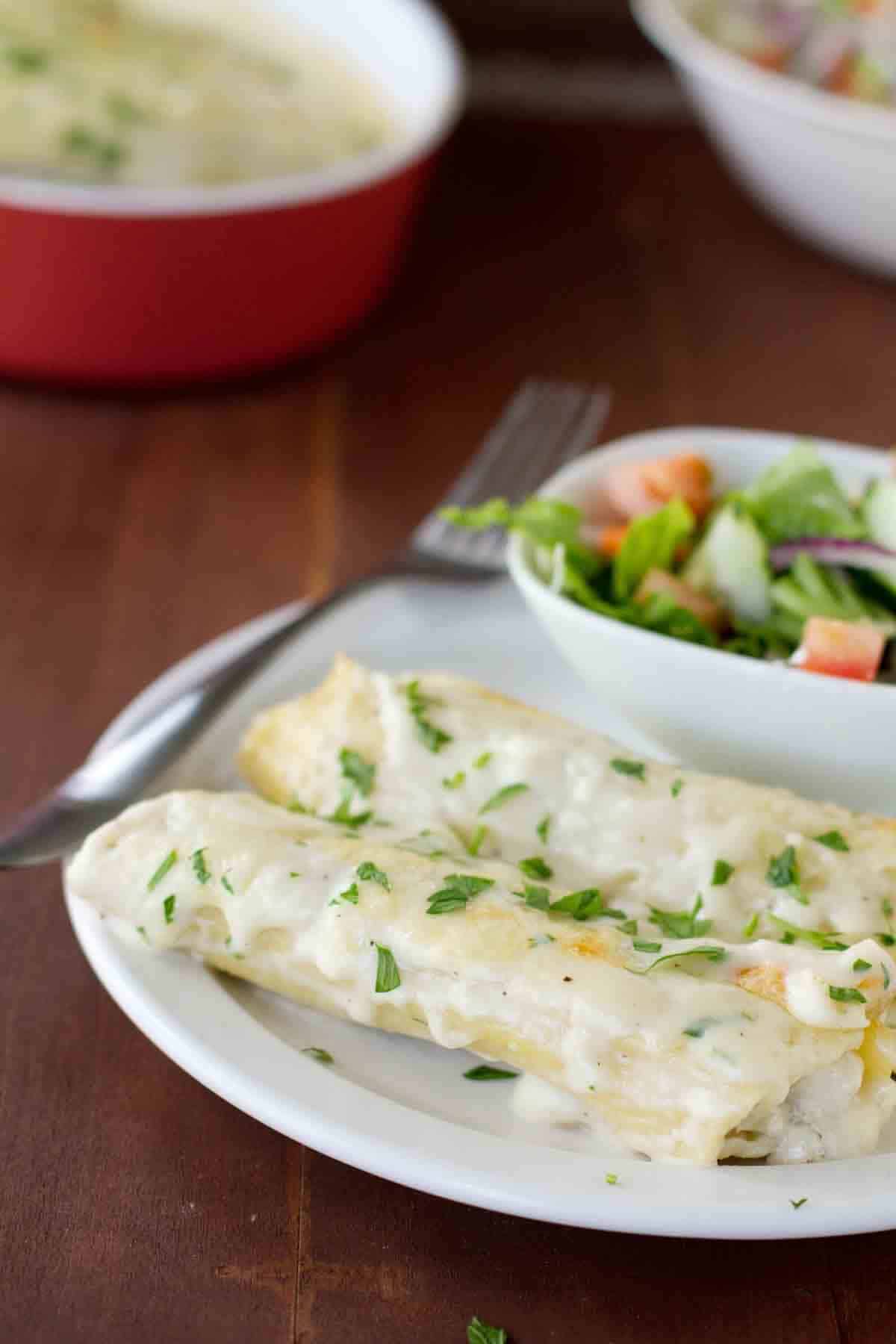 Chicken Manicotti with Mushrooms on a plate with a side salad in the background.