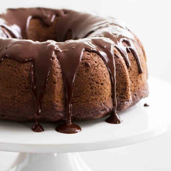 full chocolate bundt cake with chocolate icing on a white cake stand.