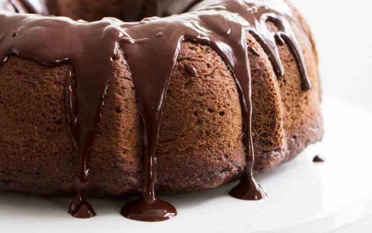 full chocolate bundt cake with chocolate icing on a white cake stand.