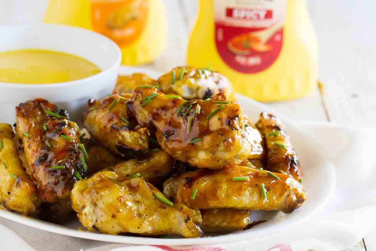 Maple Mustard Grilled Chicken Wings on a plate with mustard sauce in the background.