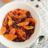 bowl of orange compote with candied cranberries with a serving spoon.