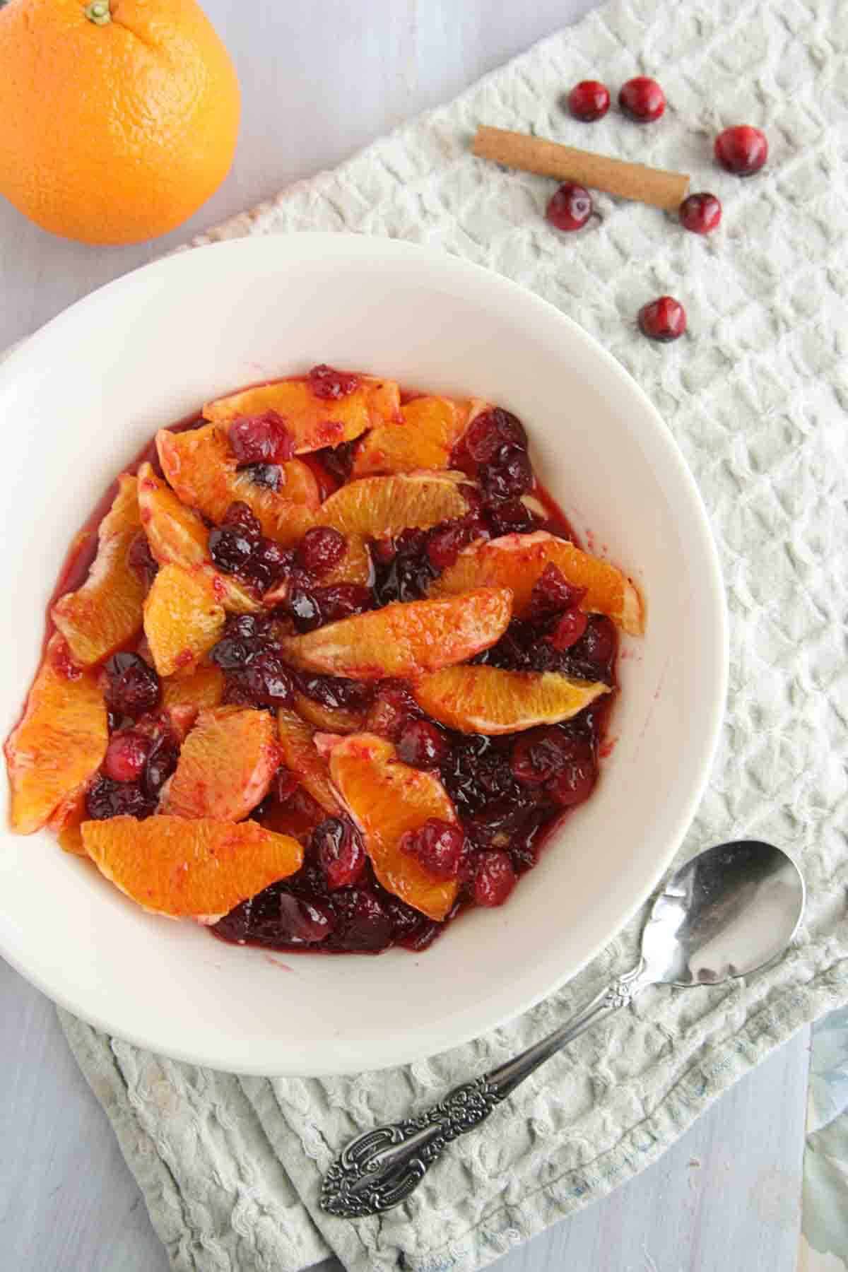 bowl of orange compote with candied cranberries with a serving spoon.