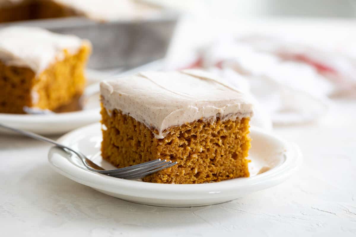 Slice of pumpkin cake with cinnamon cream cheese frosting on a plate.
