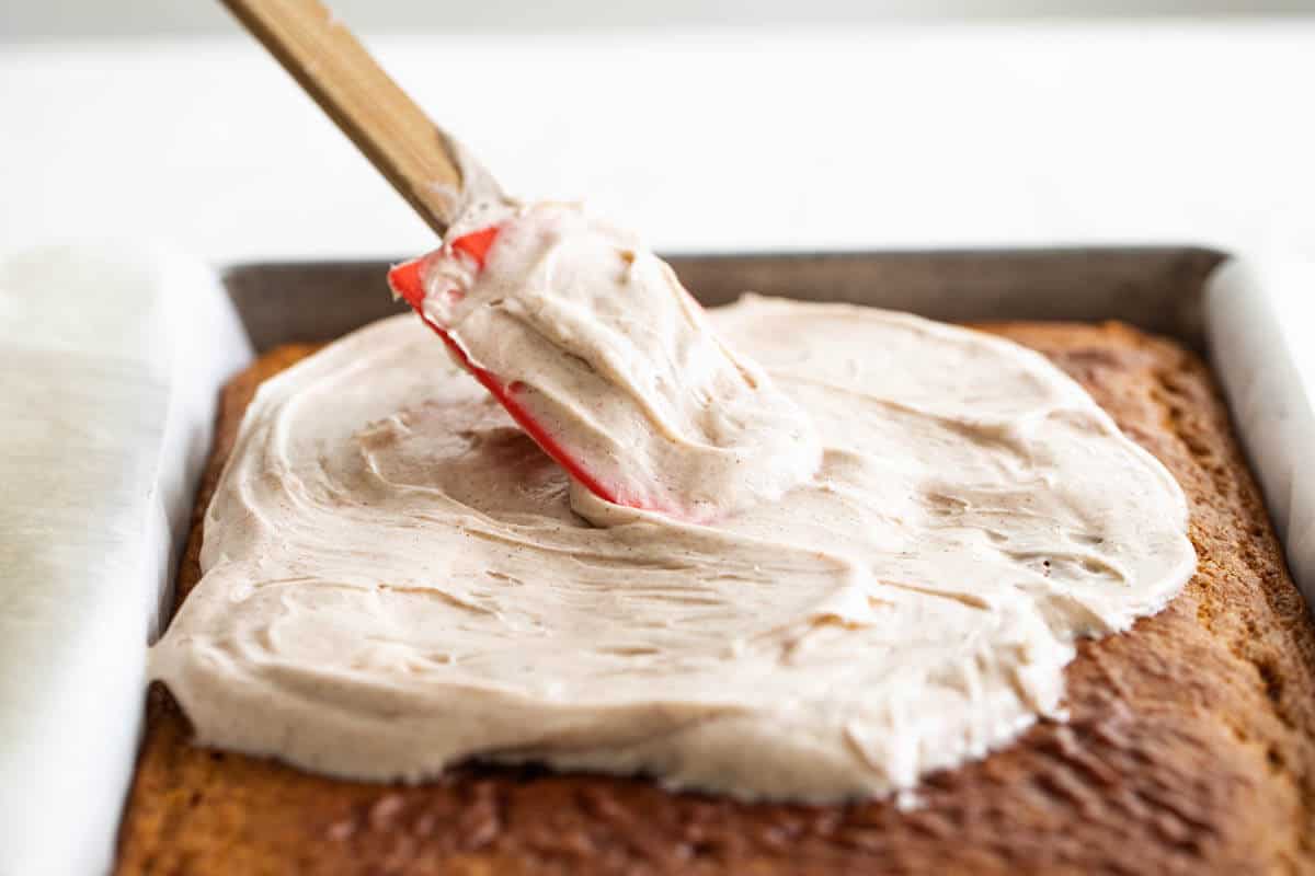 Spreading cinnamon cream cheese frosting on top of a pumpkin cake.