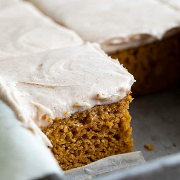 pumpkin cake slices in a cake pan topped with cinnamon cream cheese frosting.