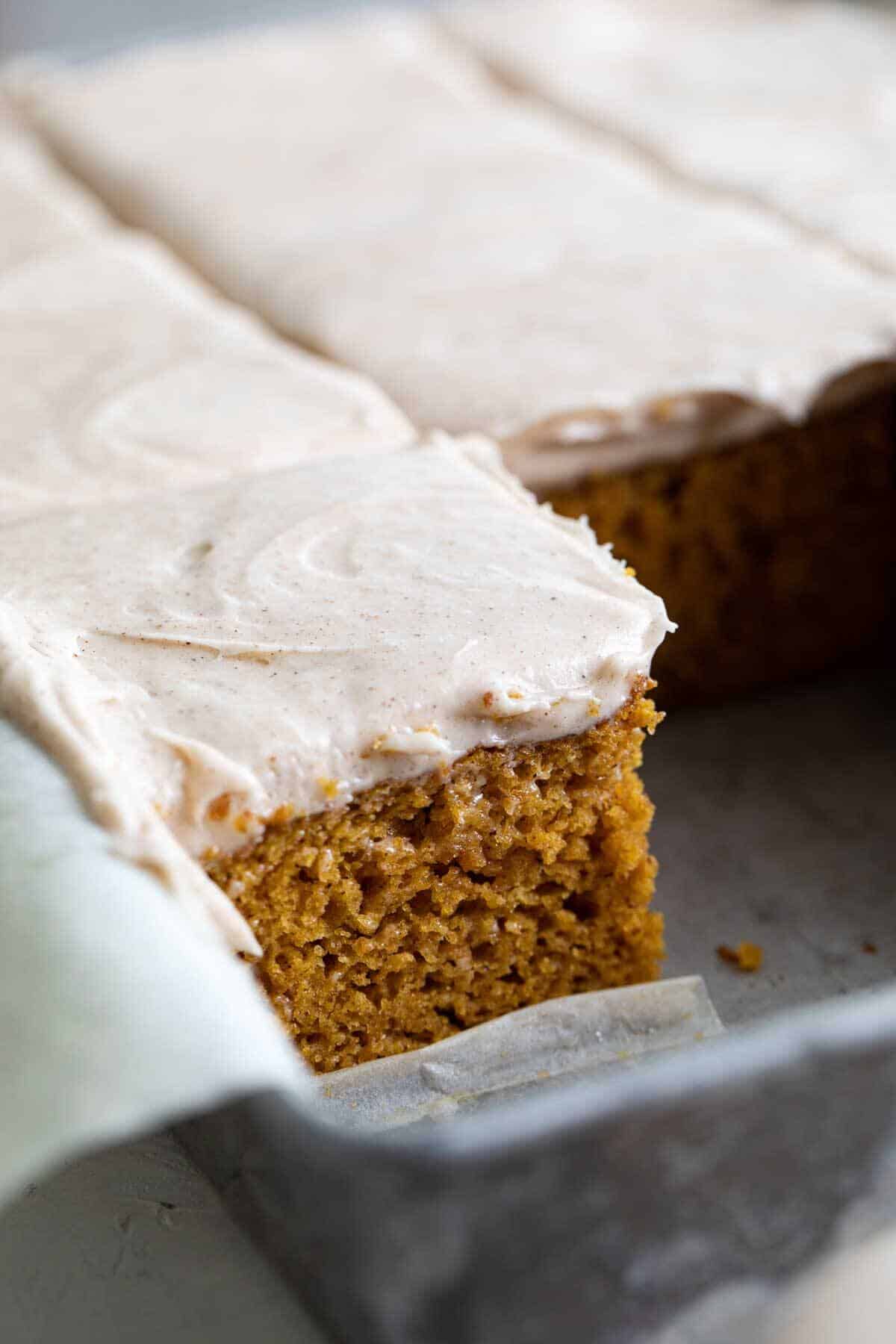 pumpkin cake slices in a cake pan topped with cinnamon cream cheese frosting.