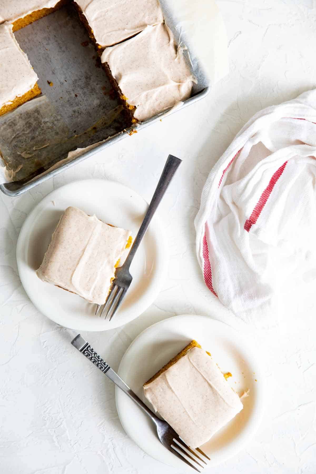 two slices of pumpkin cake on plates with the pan of cake in the back.