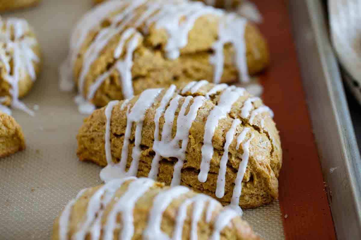 Pumpkin scones with icing on a baking sheet.