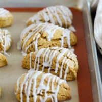 Pumpkin scones with icing on a baking sheet.