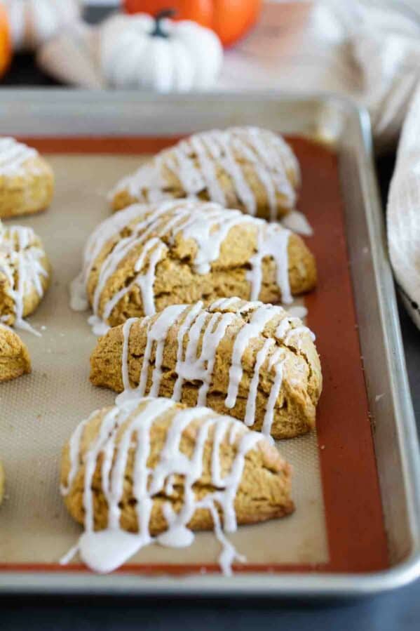 Pumpkin scones with icing on a baking sheet.