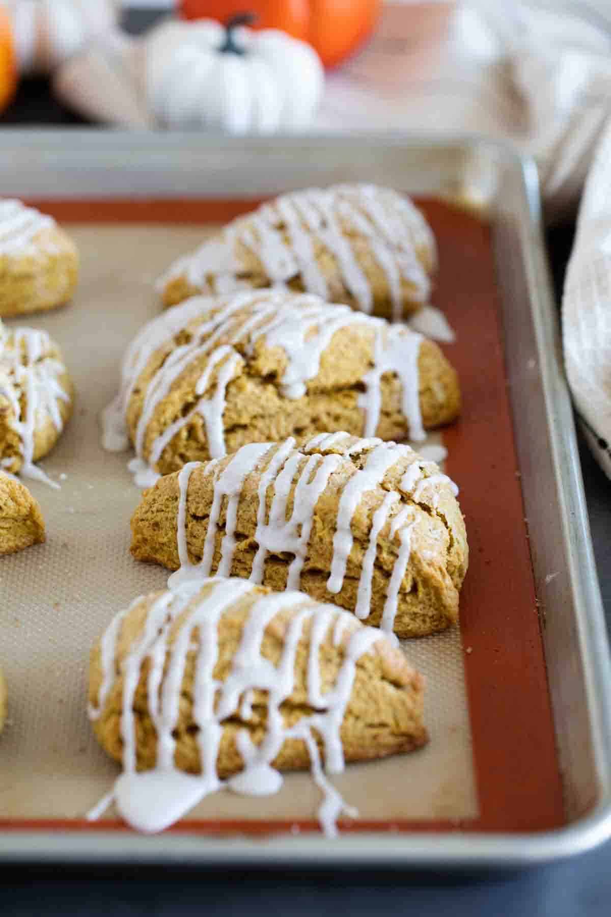 Pumpkin scones with icing on a baking sheet.