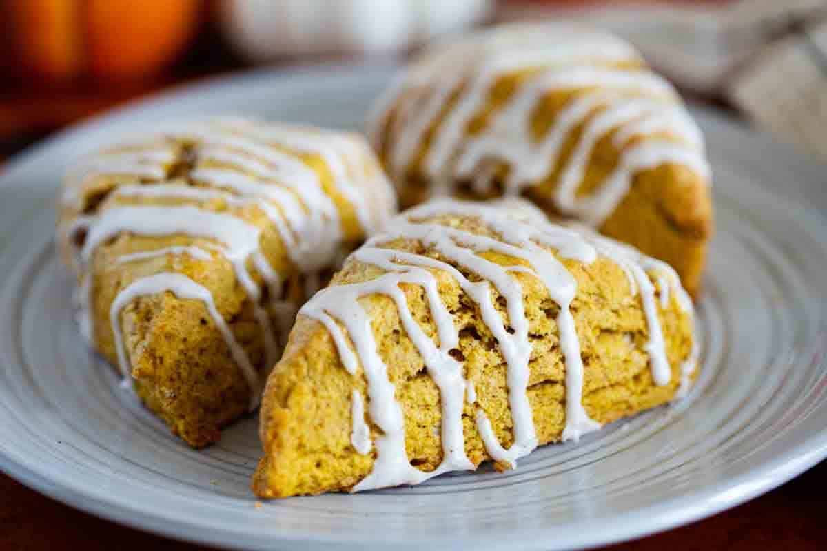 Three iced pumpkin scones on a plate.