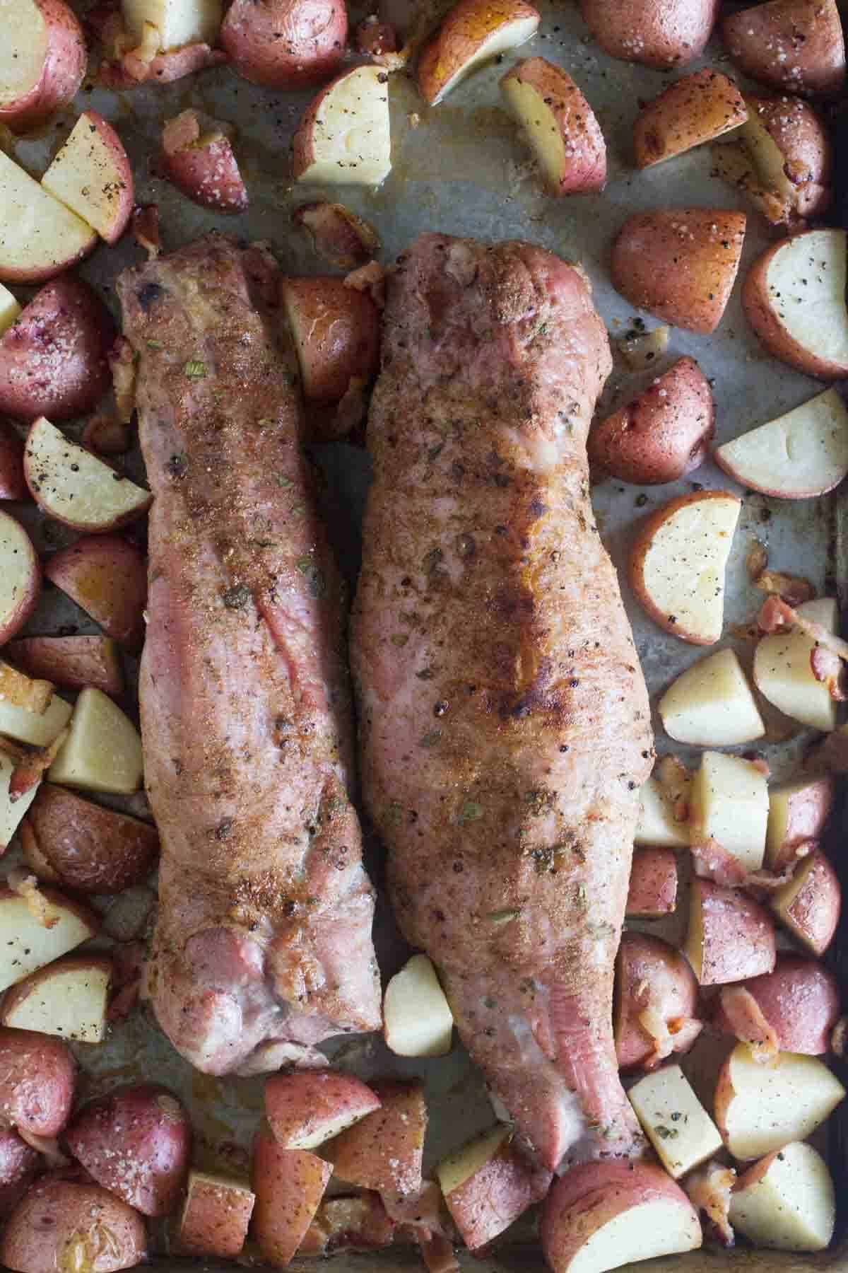 Two pork tenderloins with potatoes on a baking sheet.