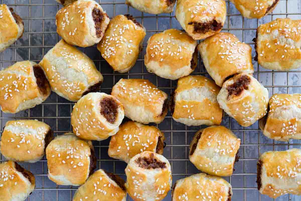 Lots of sausage rolls on a cooling rack stacked next to each other.