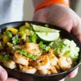 Hands holding a bowl filled with shrimp, rice, pineapple, mango, and avocado.