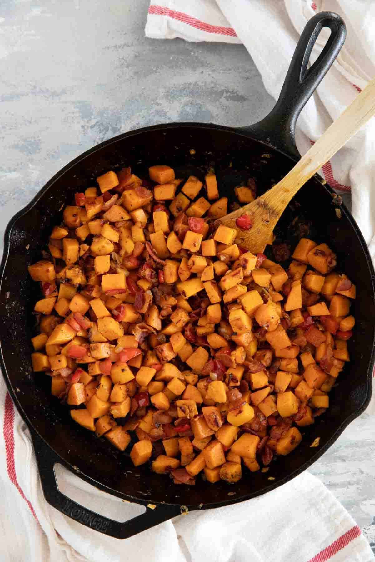 Cast iron skillet with sweet potato hash with bacon and red peppers.