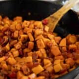 Wooden spoon in a skillet full of sweet potato hash.