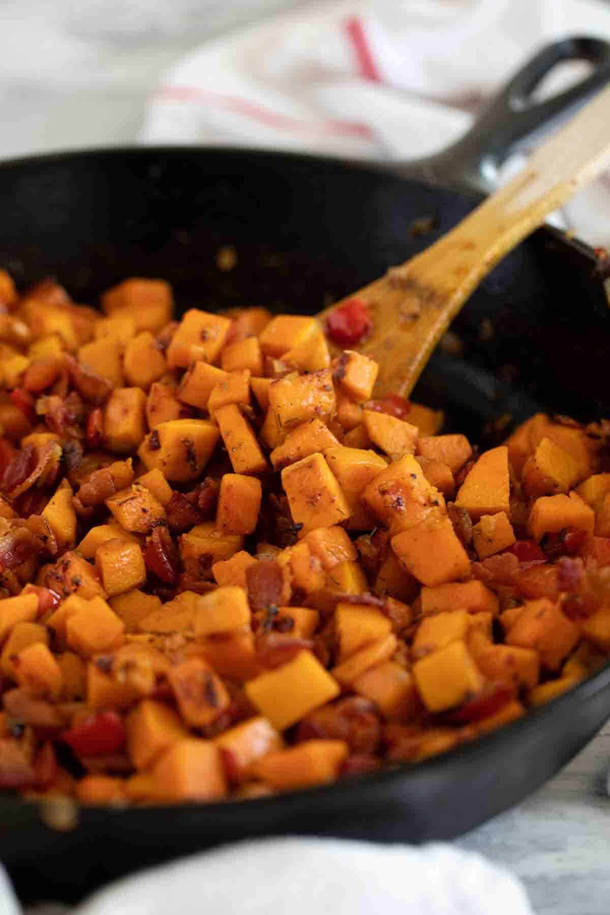 Wooden spoon in a skillet full of sweet potato hash.