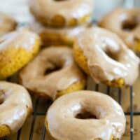 Baked pumpkin donuts stacked on a cooling rack.