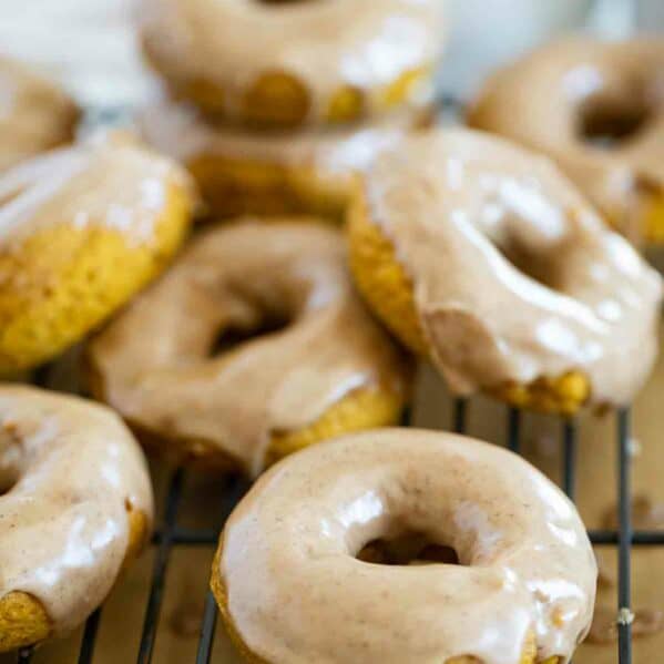 Baked pumpkin donuts stacked on a cooling rack.