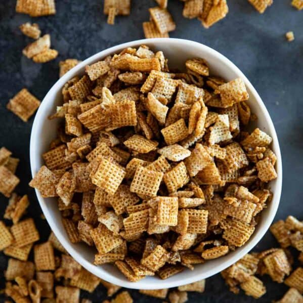 Bowl full of cinnamon caramel snack mix with more outside the bowl.