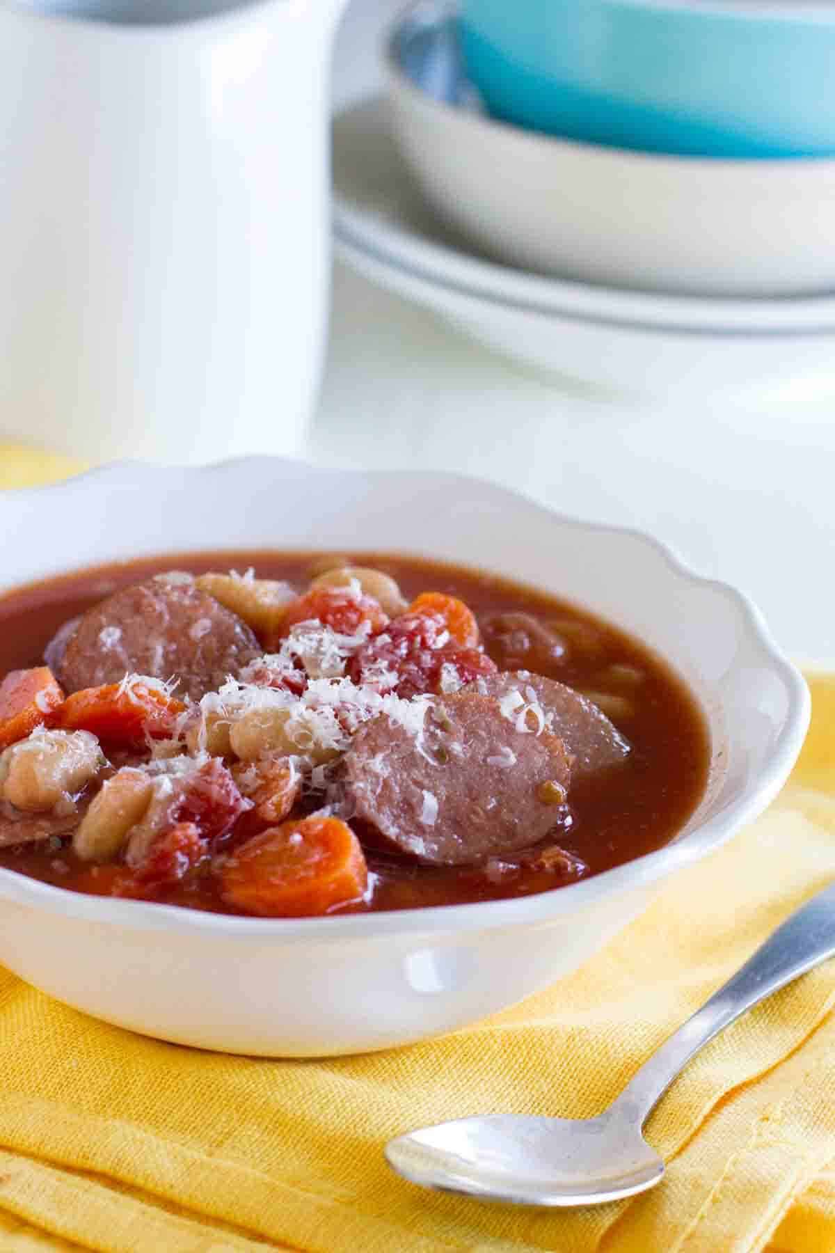 Bowl of slow cooker white bean soup with sausage on a yellow napkin.