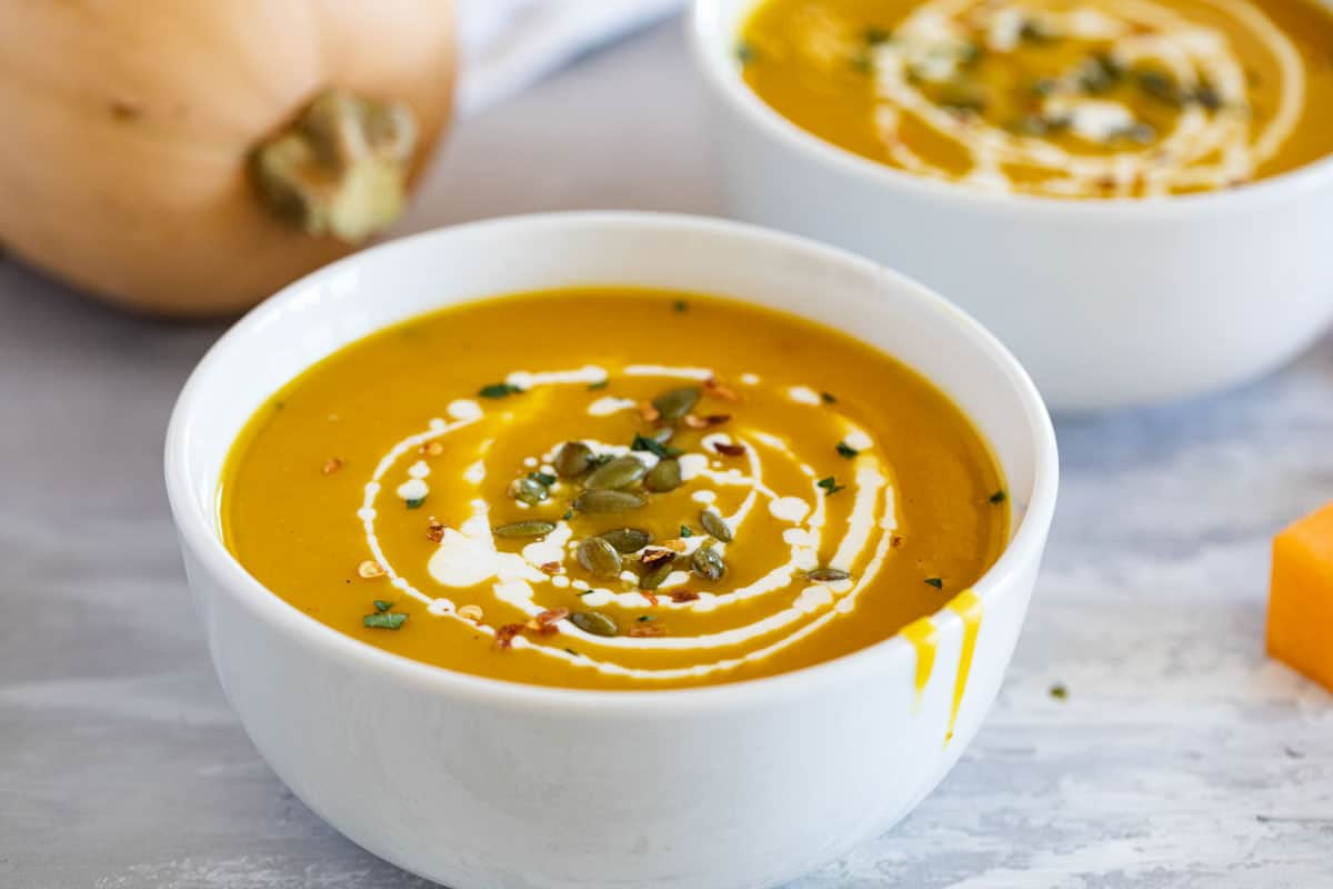 Two bowls of curried butternut squash soup that have been topped with cream and pepitas.