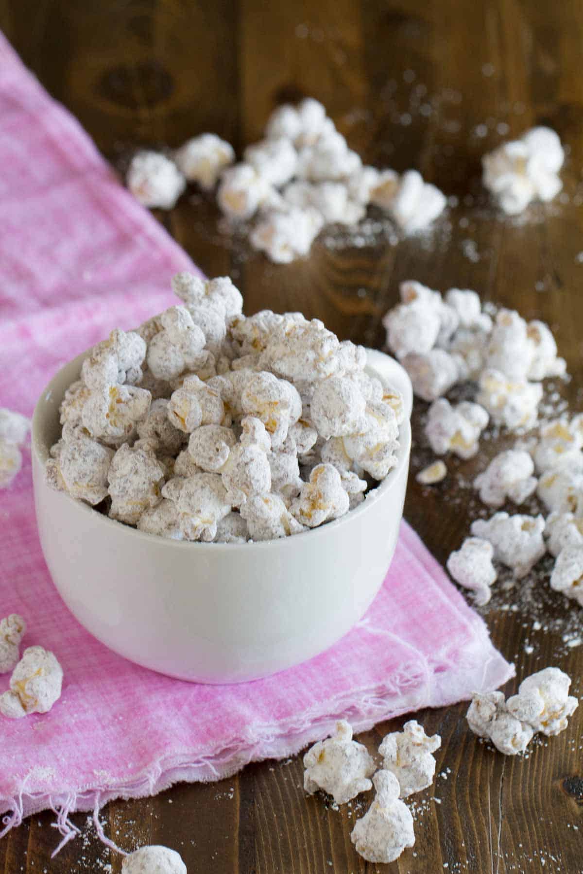 Bowl of muddy buddy popcorn with popcorn spilled around the bowl.