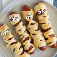 Mummy hot dogs with candy eyes on a plate.