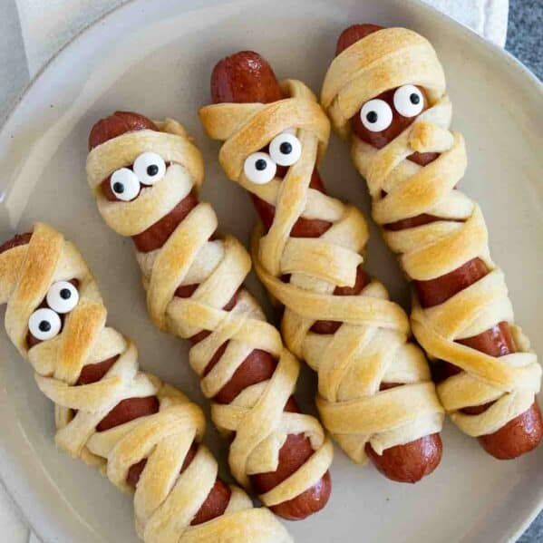 Mummy hot dogs with candy eyes on a plate.