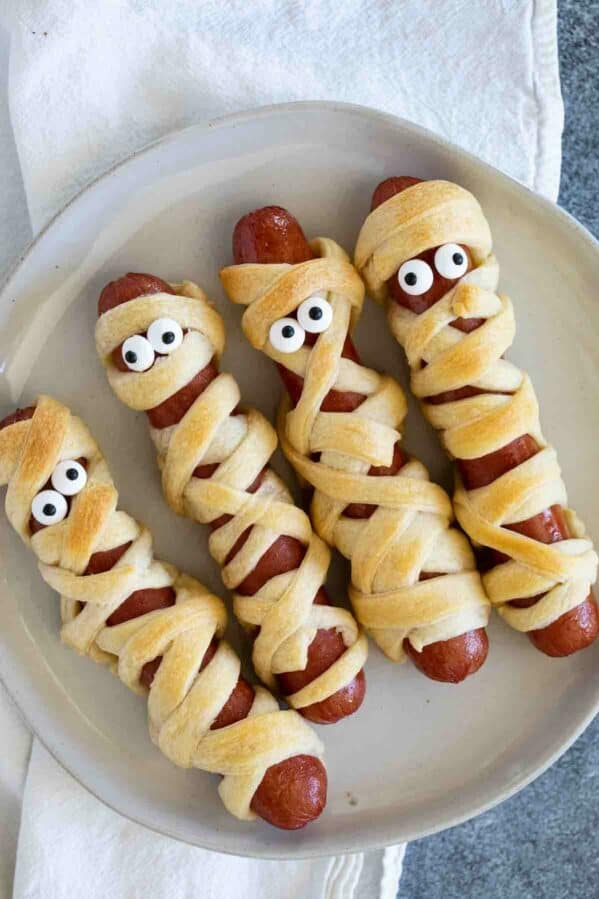 Mummy hot dogs with candy eyes on a plate.