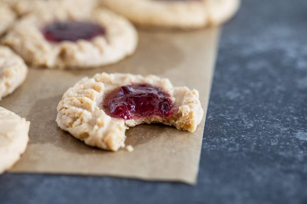 Peanut Butter and Jelly Thumbprint Cookies on parchment paper with a bite taken from one cookie.