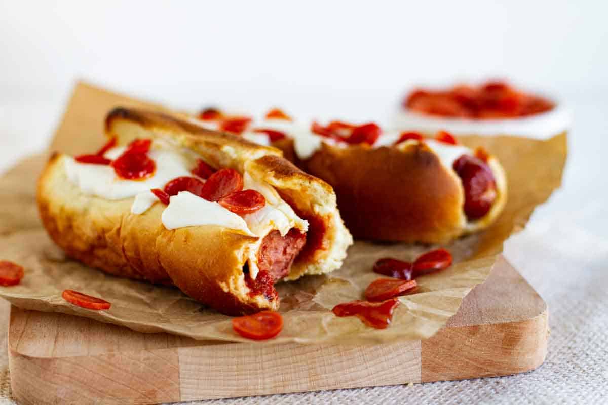 Pizza dogs on a cutting board with a bite taken from one of them.